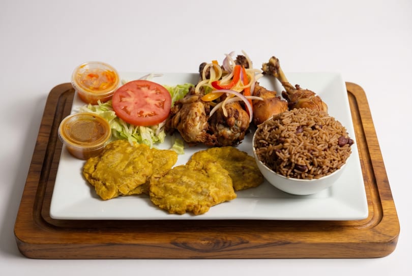 Fried chicken with rice and beans, plantains, and a side salad with dressing cups of two sauces.