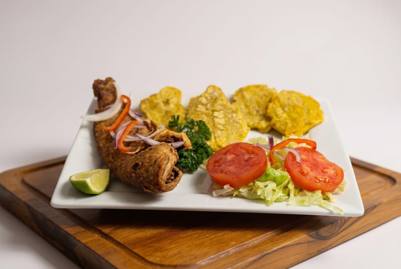 Fried fish with plantains, a side salad, and a lime wedge on a white plate.