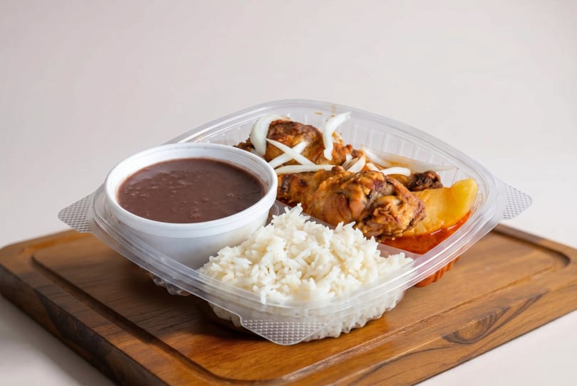 A takeout container with chicken, rice, beans, and potatoes on a wooden board.
