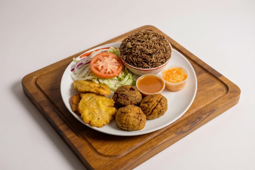 A plate of rice, salad, fried plantains, and meat croquettes with two dipping sauces on a wooden board.